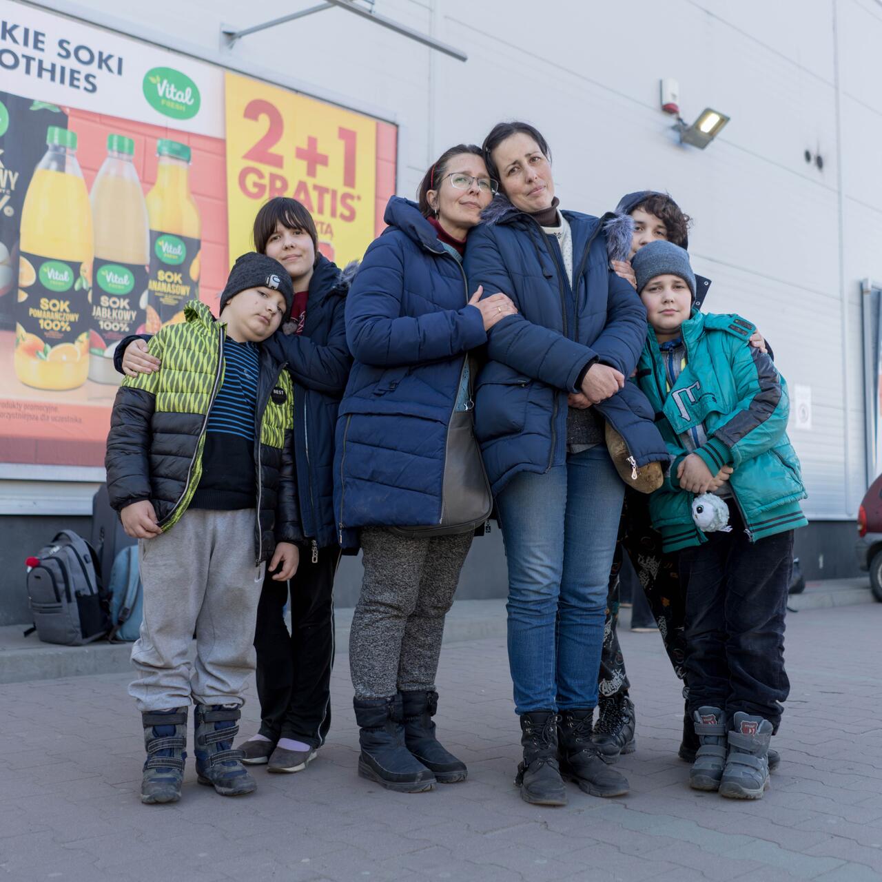 Two women surrounded by their children, all are wearing winter clothes and looking at the camera.