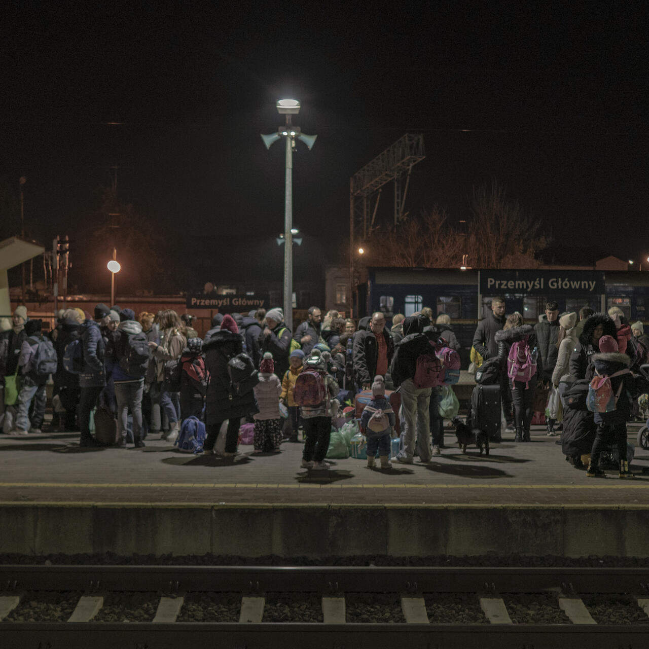 A group of many people stand outside on a train station platform.