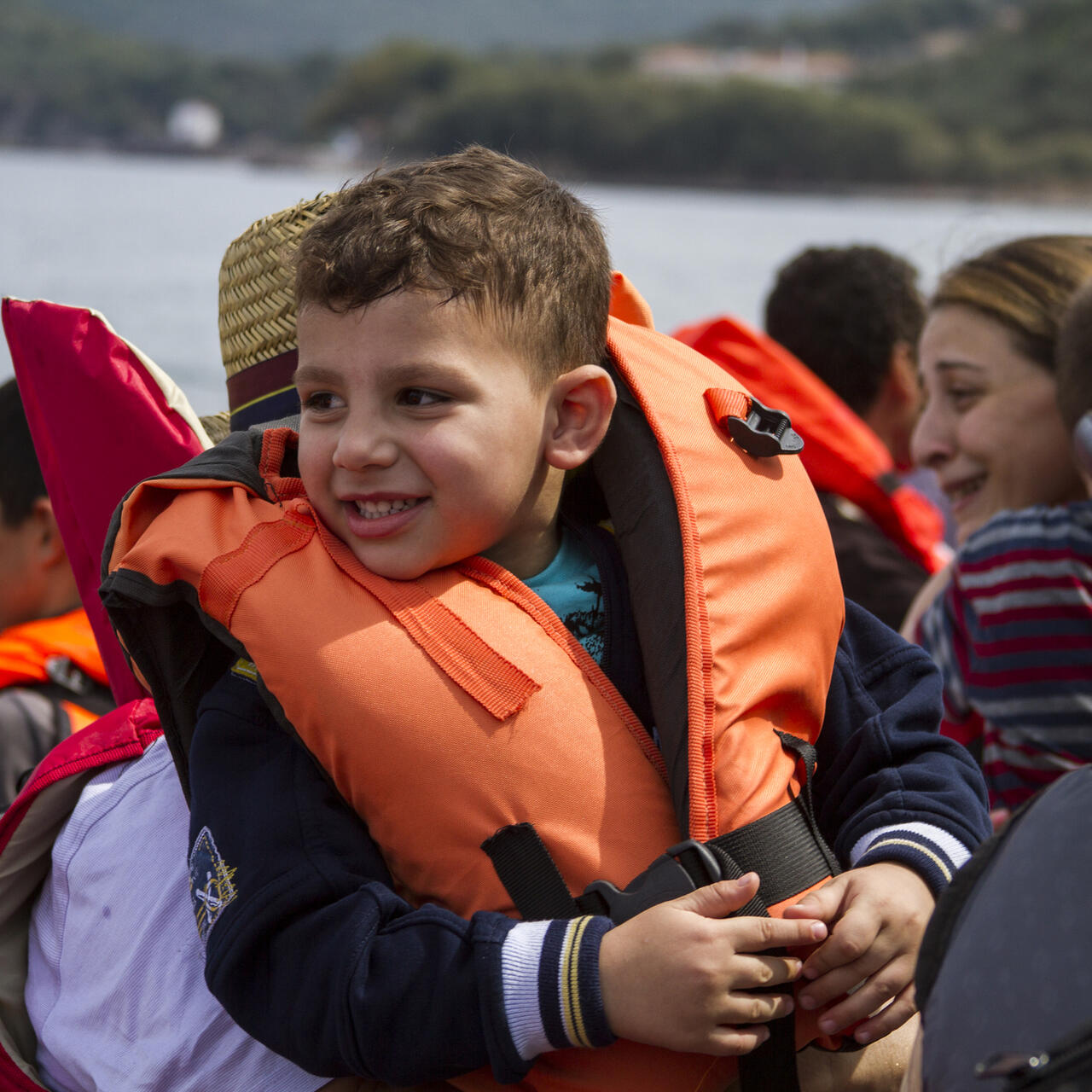 A small boy wearing a life vest nears the Greek coast in a rubber raft overflowing with other refugees.