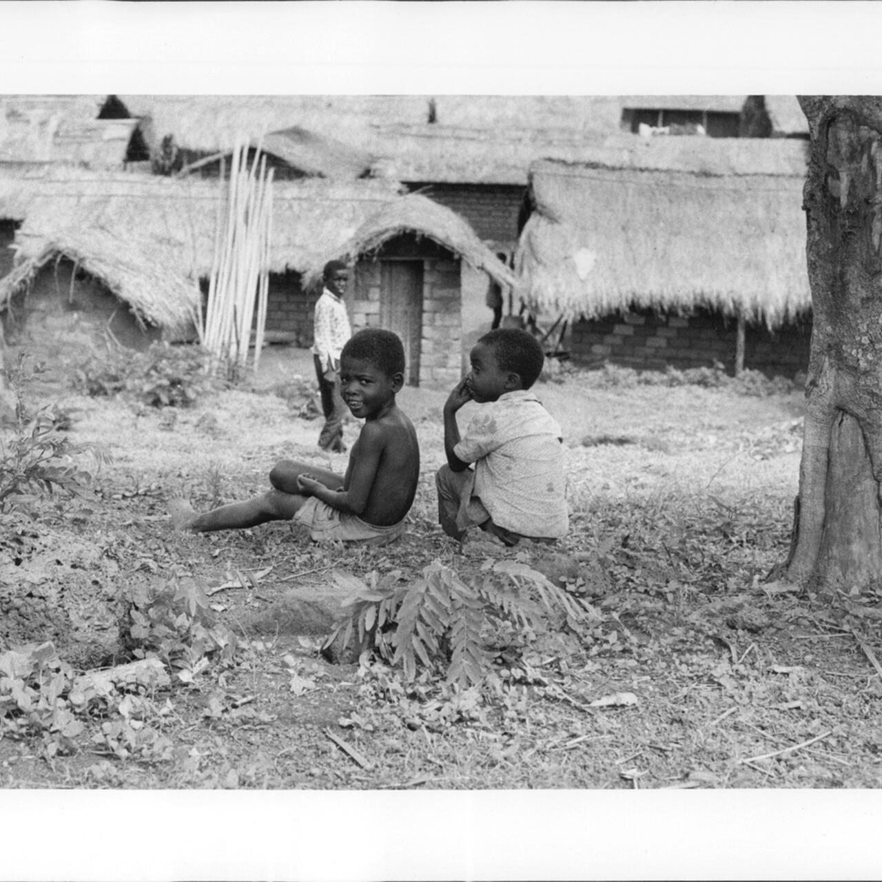 Angolan refugee children sit on the ground outside a row of houses in Zaire.