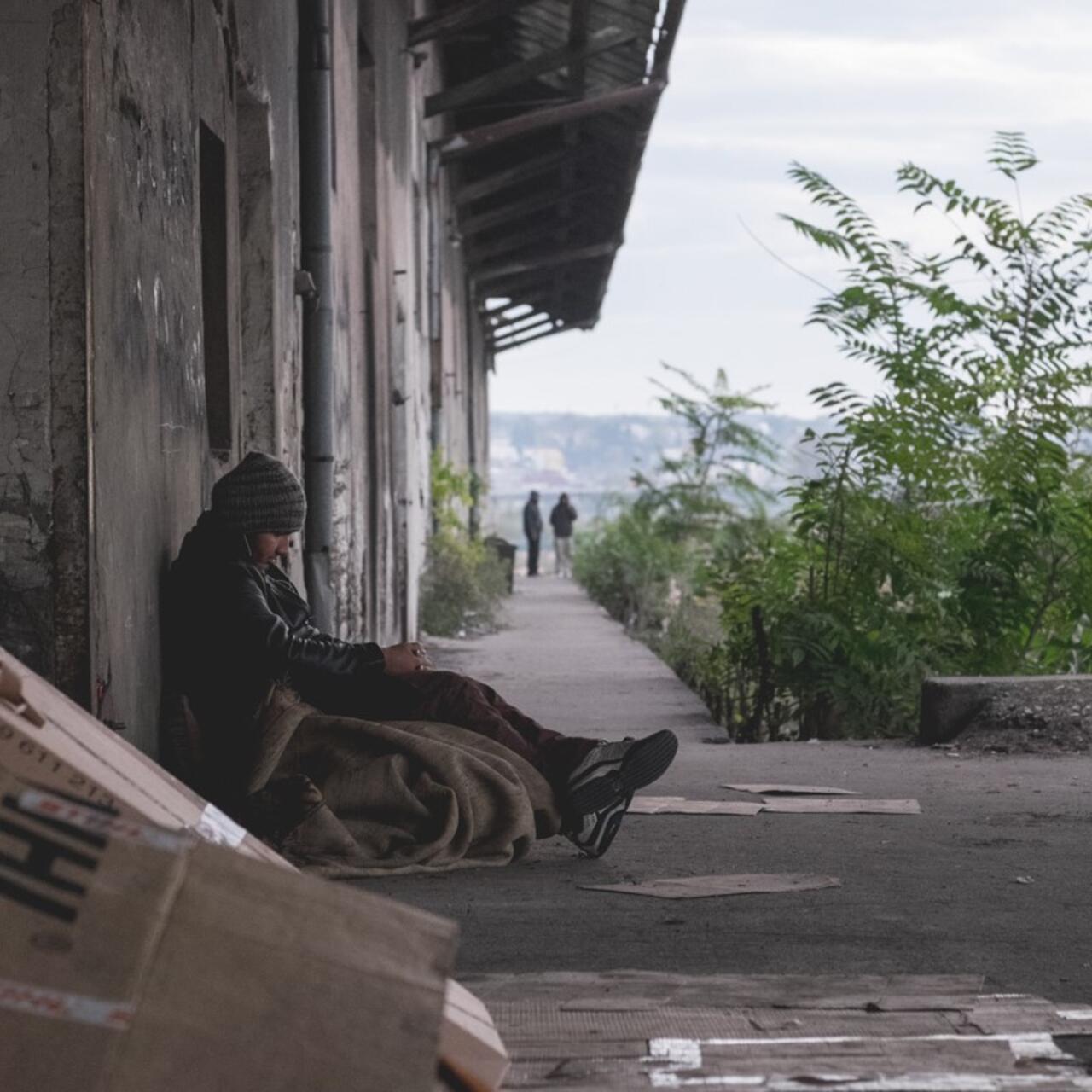 A young Afghan refugee sits huddled outside an abandoned warehouse in Serbia.