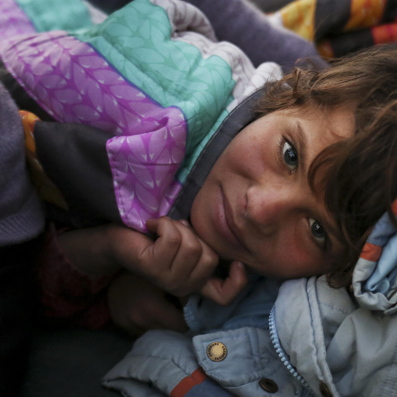 A Syrian refugee girl stays warm in blankets inside a tent in Greece