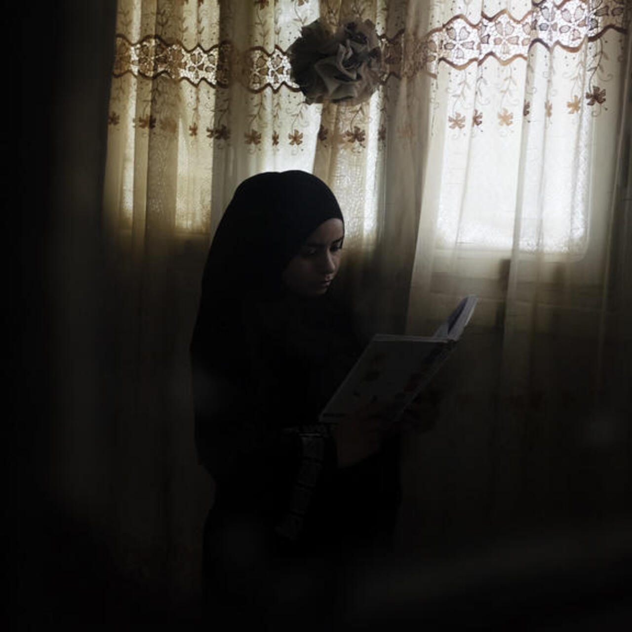 Rawan sits by a window, reading