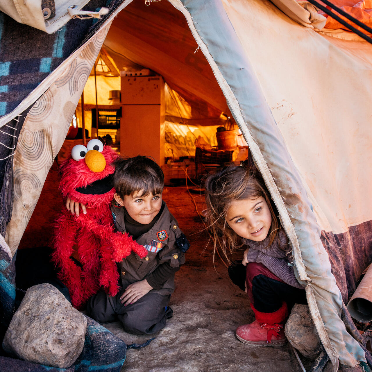 A young Syrian boy and girl  with a Sesame Street Elmo puppet in their tent in a refugee camp in Jordan