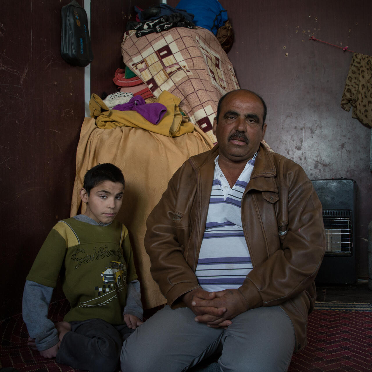 Abu Raed sits with his son Bashar, who is paralyzed, in their family's caravan at the Zaatari refugee camp in Jordan.