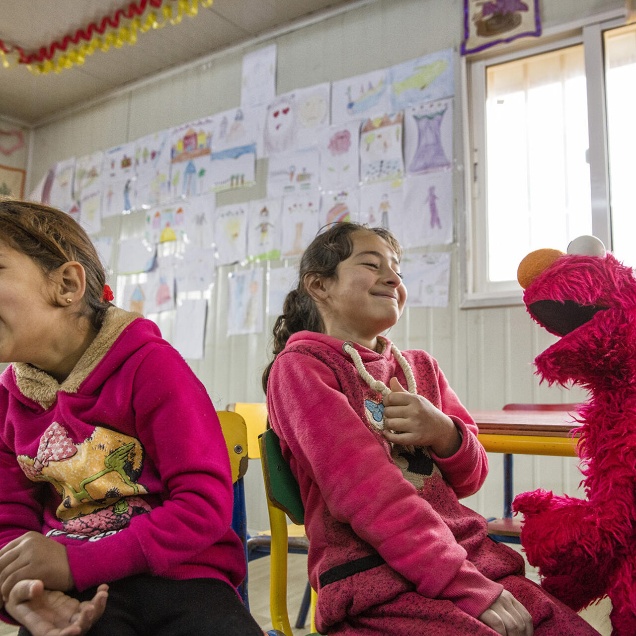 Two Syrian girls laugh as they play with Sesame Street Muppet Elmo
