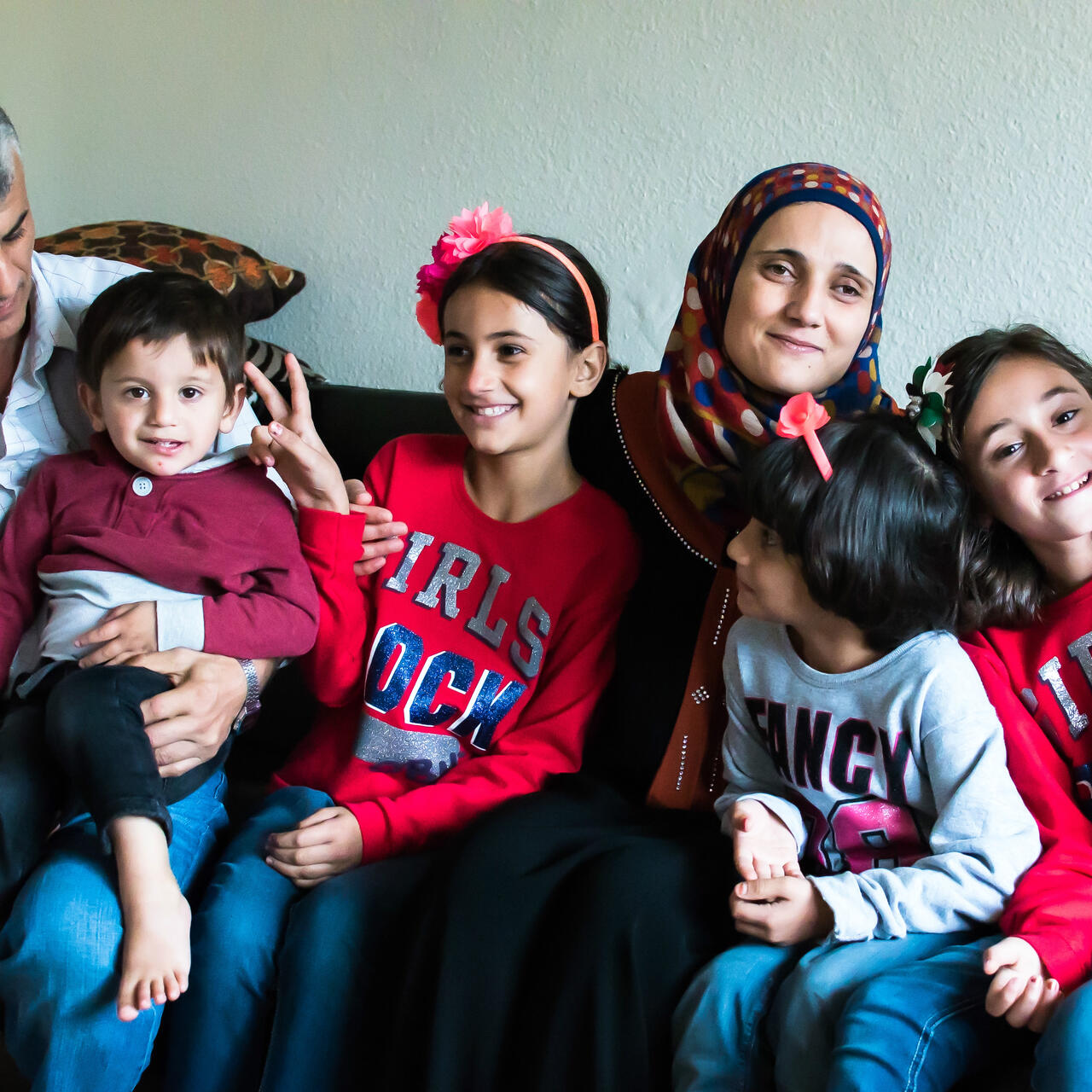 The Tlases and their four children pose for a family photo on their couch.