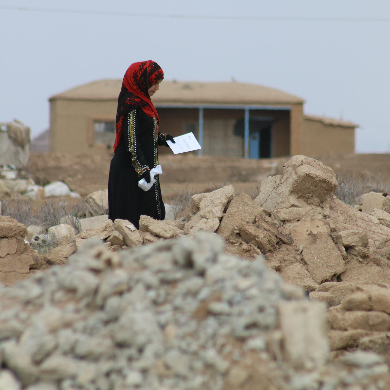 A woman picks her way through the rubble of her village in Northeast Syria, carrying a bag of prescription medicine that she received from an IRC mobile clinic.