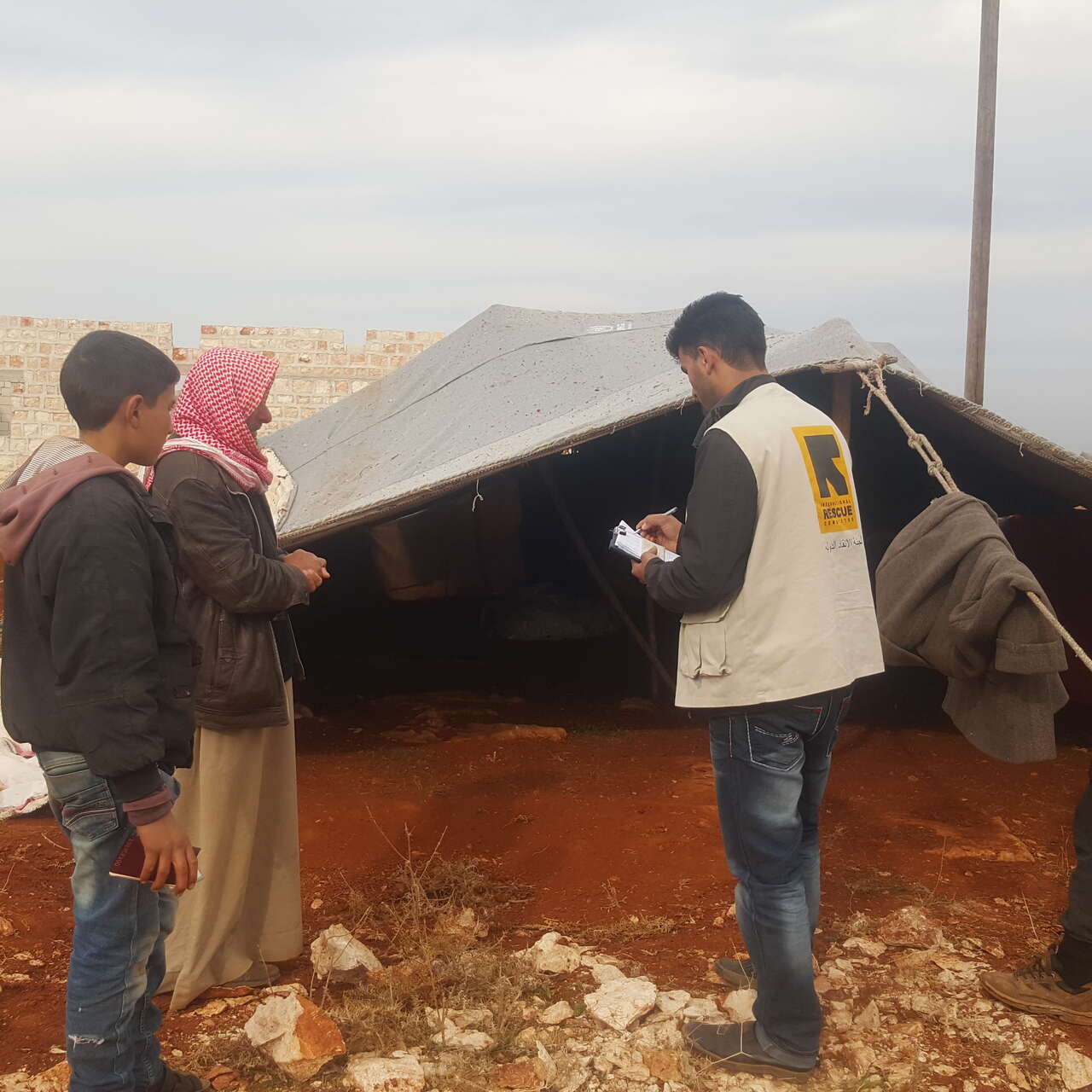 An IRC aid worker speaks with a man whose family was displaced in Syrias Idlib province and living in a tent