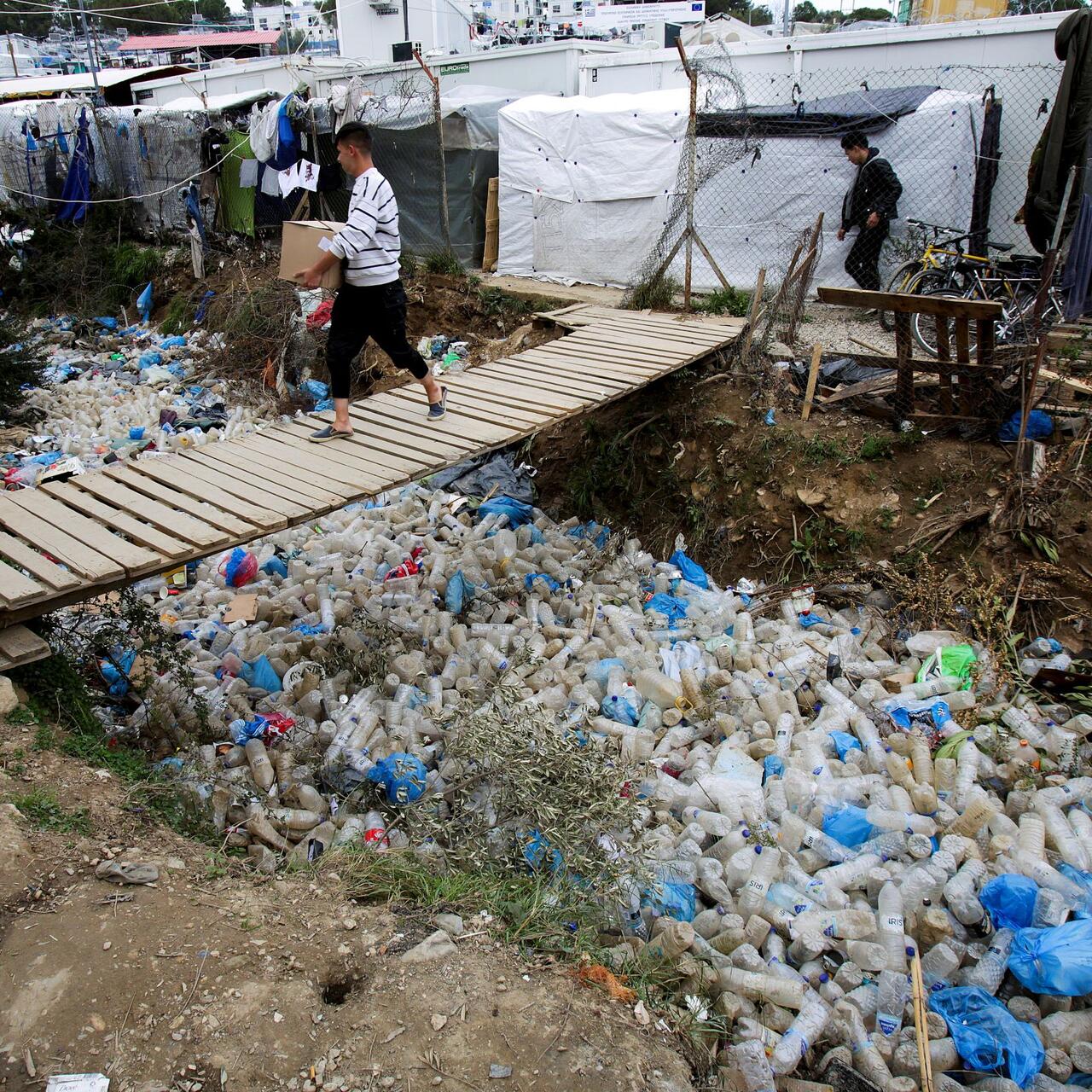 Man walking on wooden bridge under which are many discarded plastic bottles and rubbish