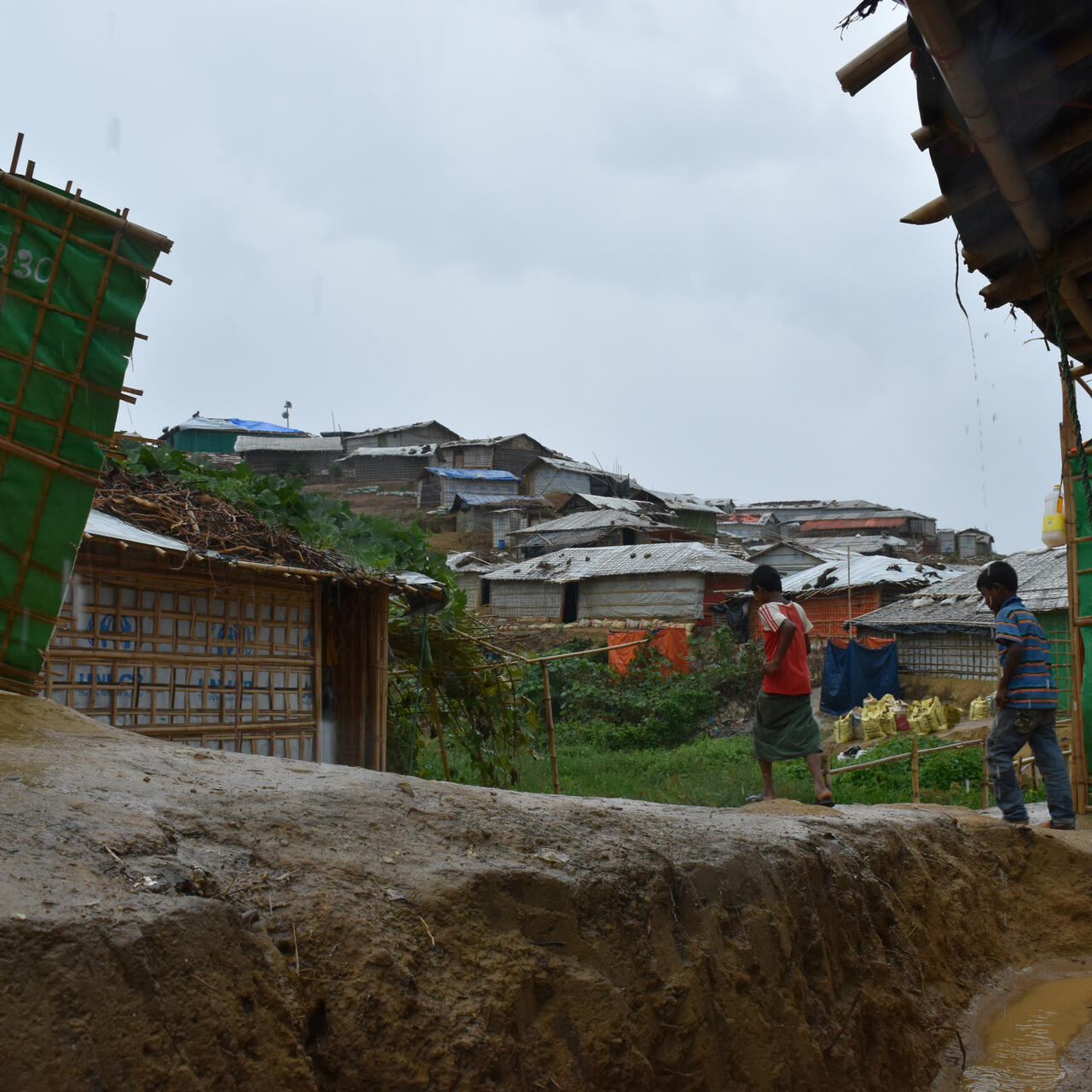 Two boys walk on muddy path through a refugee camp in Bangladesh