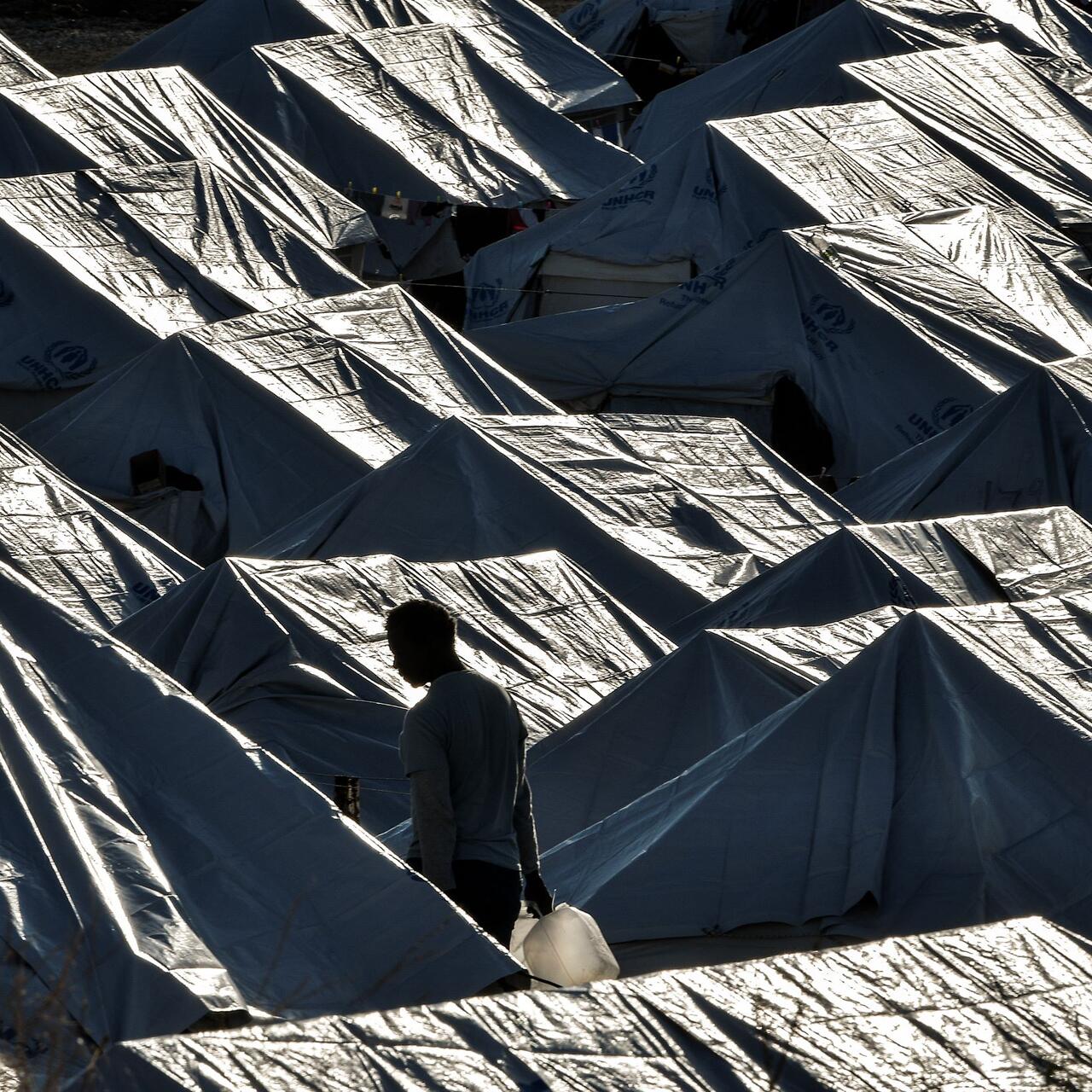 A man walks among tents with a water container