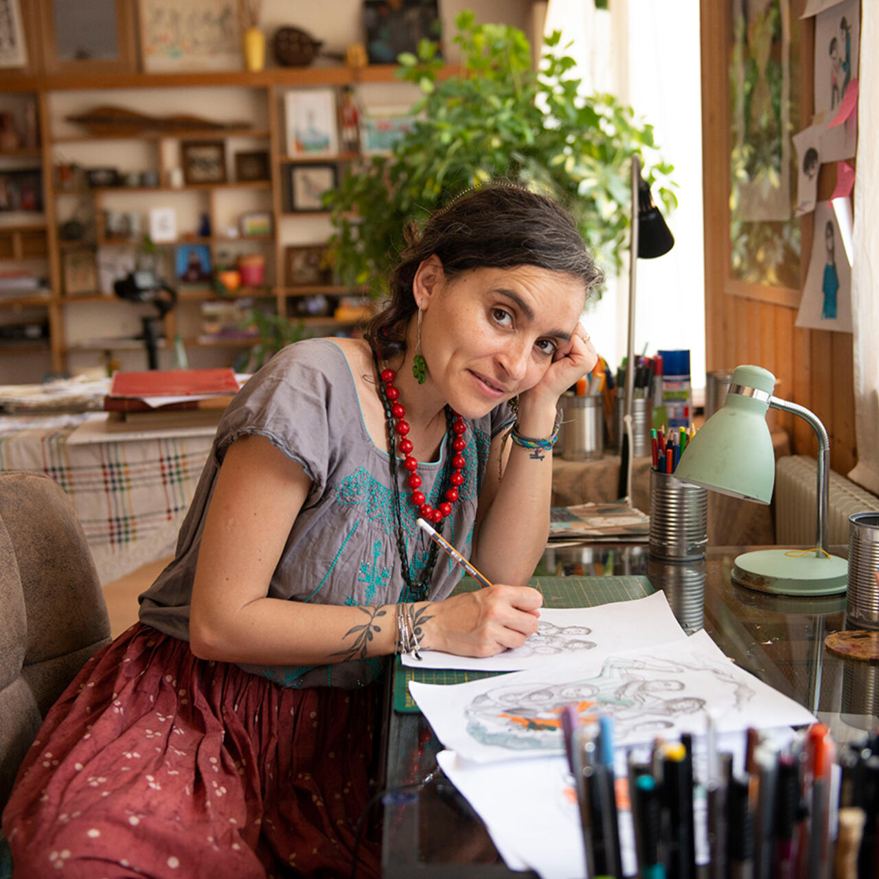Artist Diala looks up at the camera from her desk where she is designing the IRC's WRD illustration.