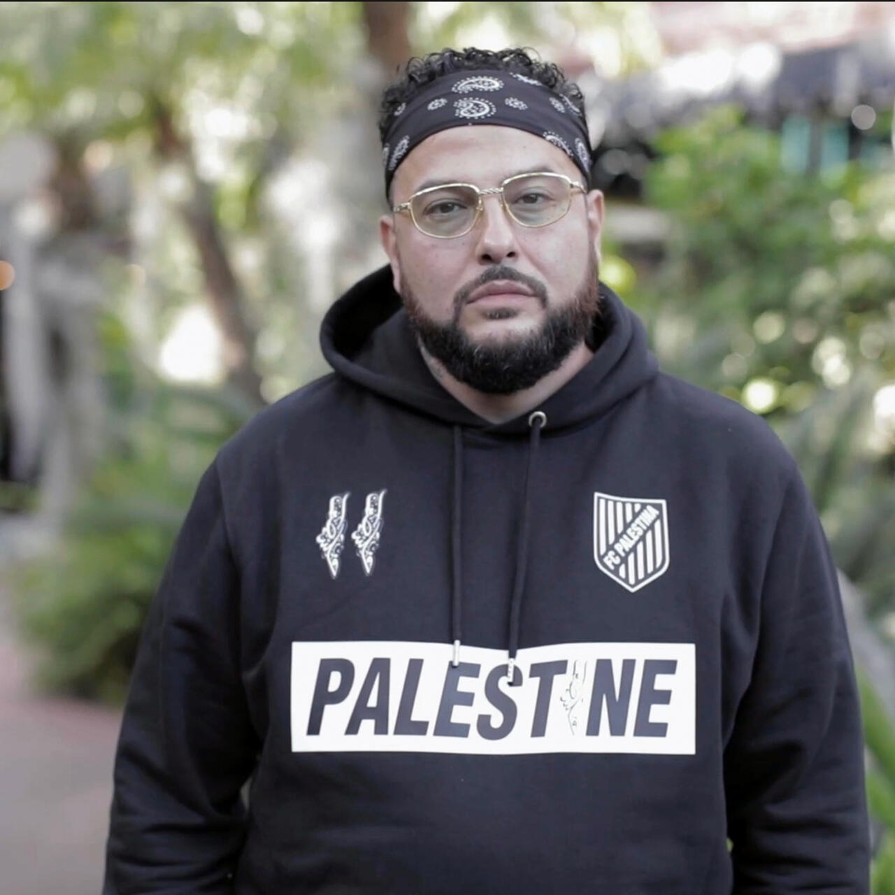 Rapper Belly stares into the camera. He is wearing a Palestine hoodie.