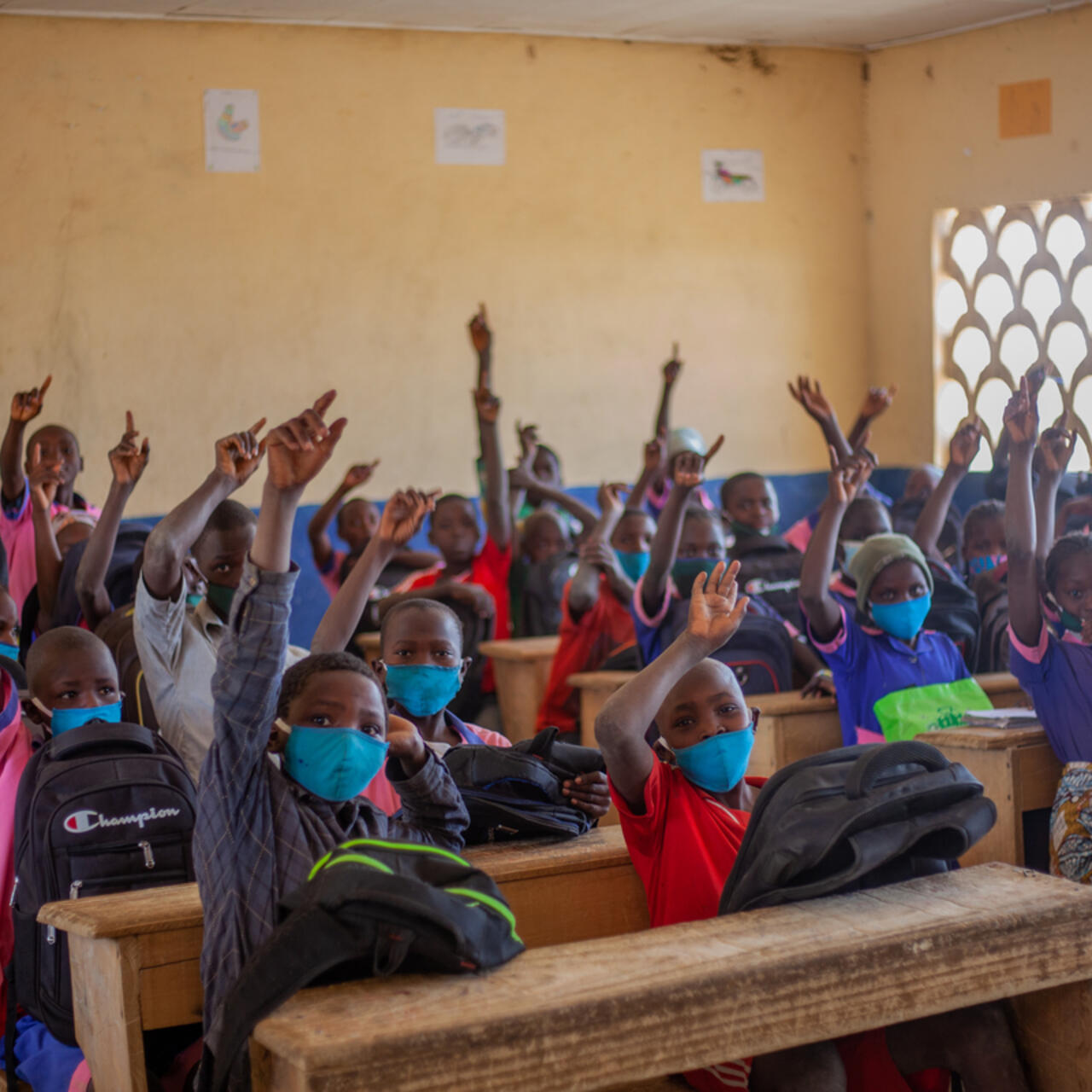 A classroom full of school children raise their hands.
