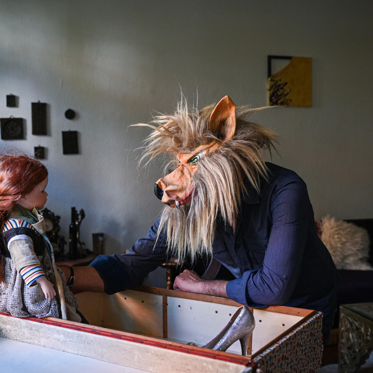 Bashar wearing a wolf mask and staring at a doll with red hair