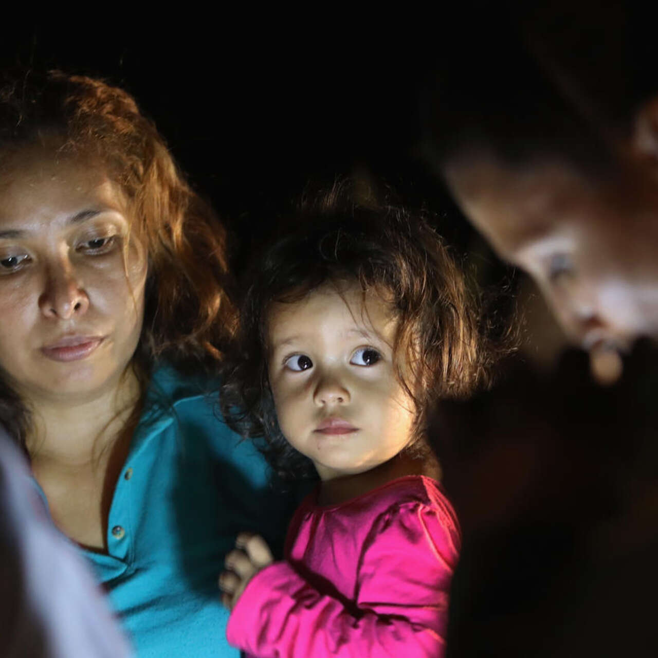 A mother holding her young daughter claiming asylum with two border control agents.