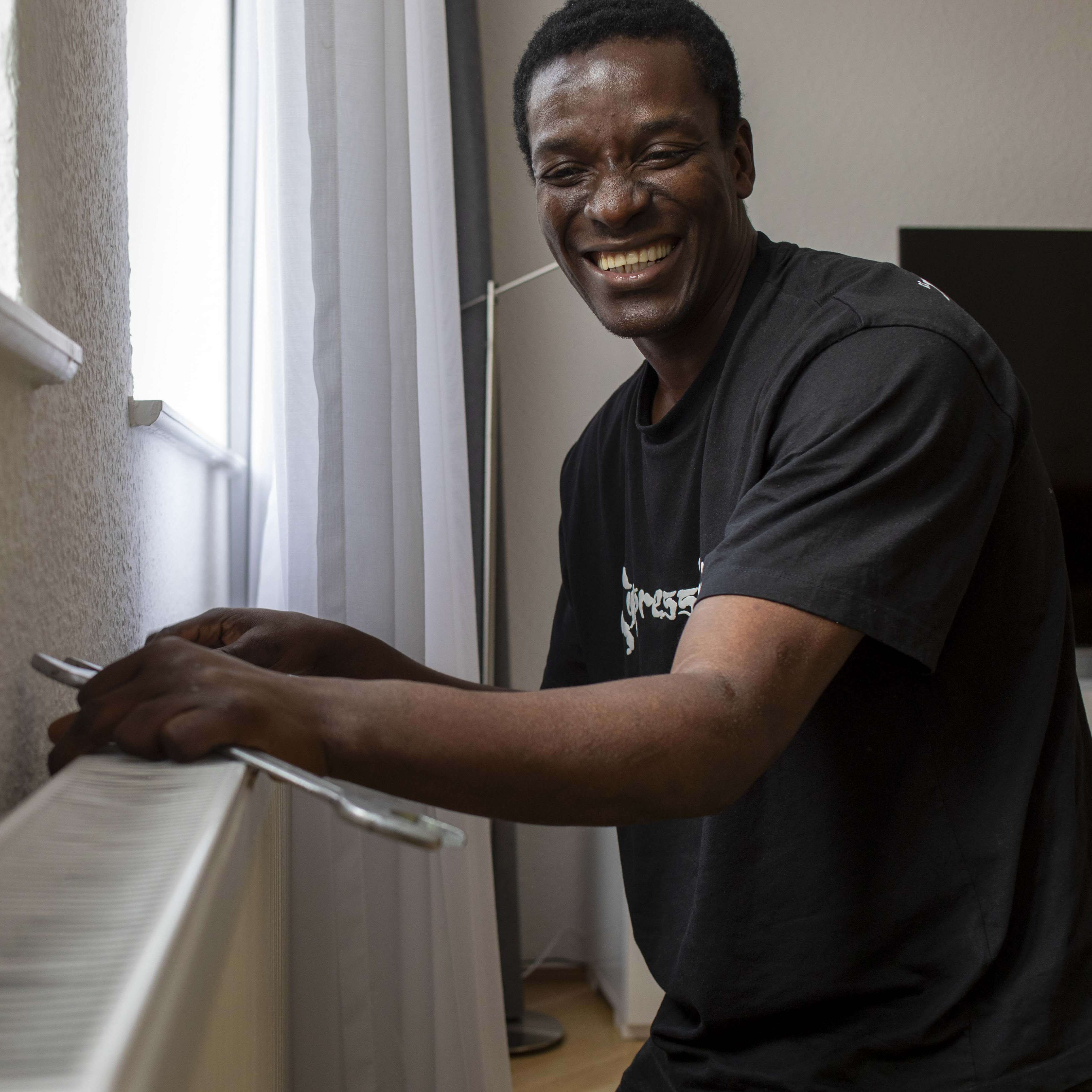 Ein lächelnder Mann arbeitet an einer Heizkörperverkleidung in einem hellen Raum.