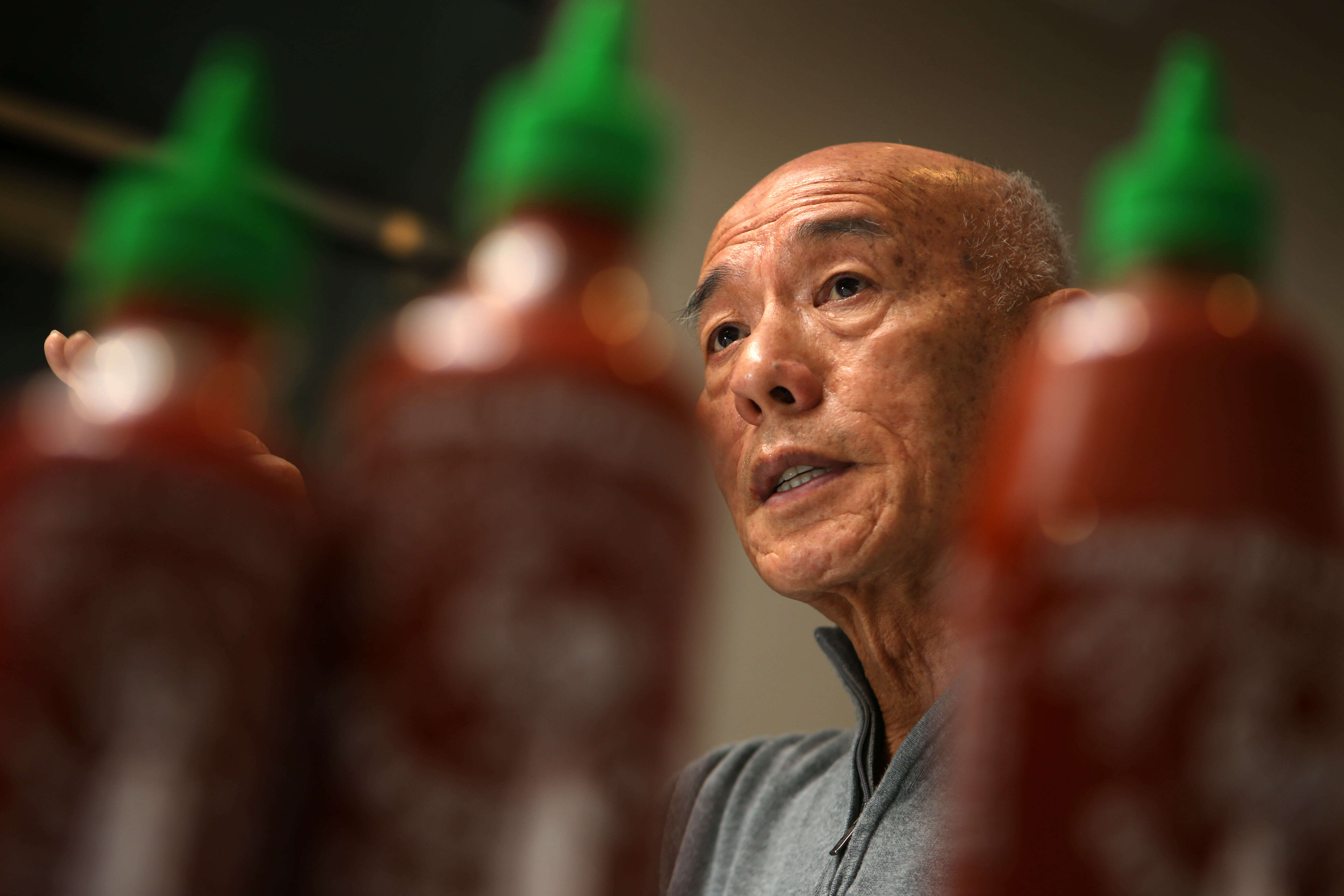 Image of David Tran focused in background, bottles of unfocussed sriracha sauce