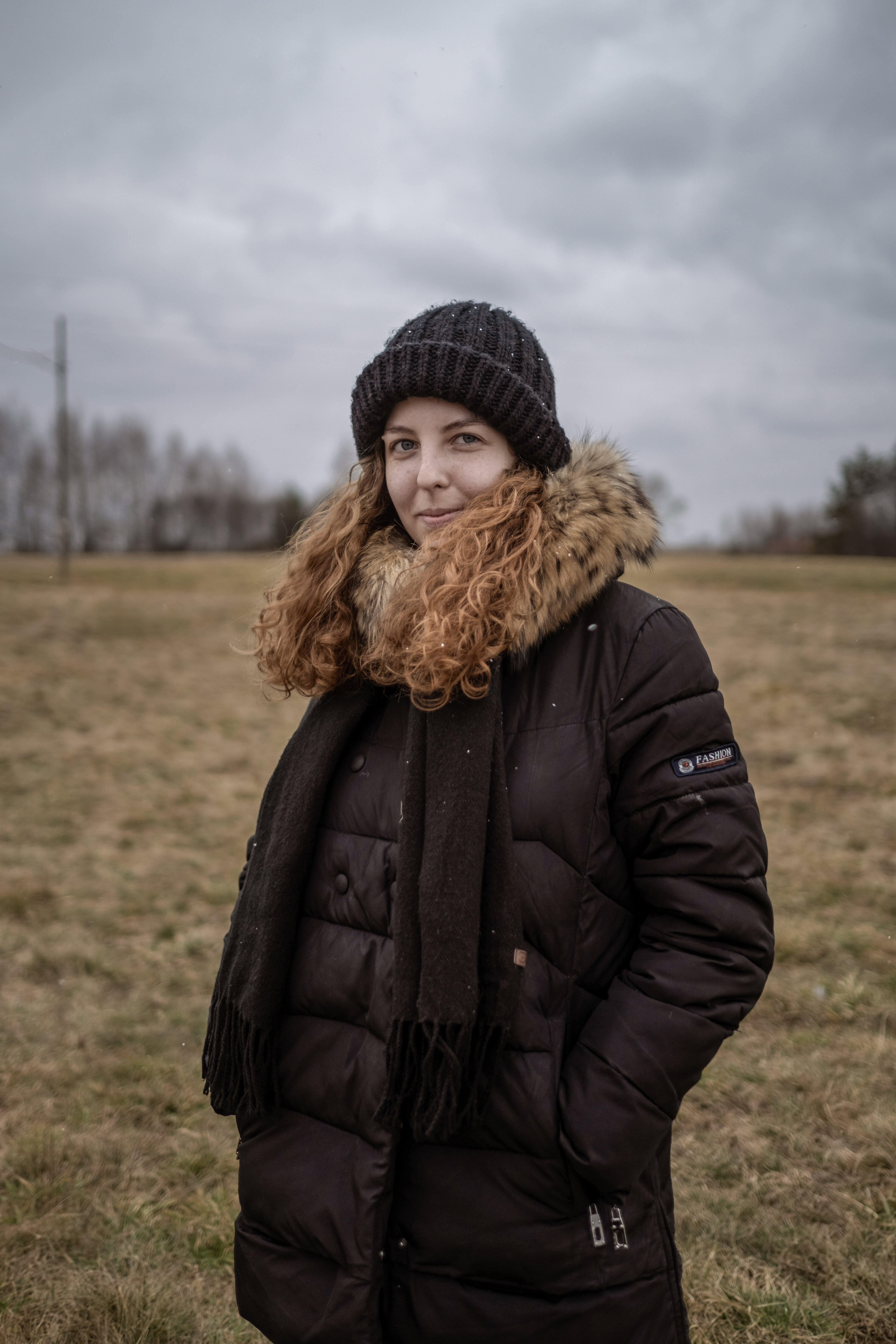 A close up of Anastasiia standing in a field wearing winter clothes