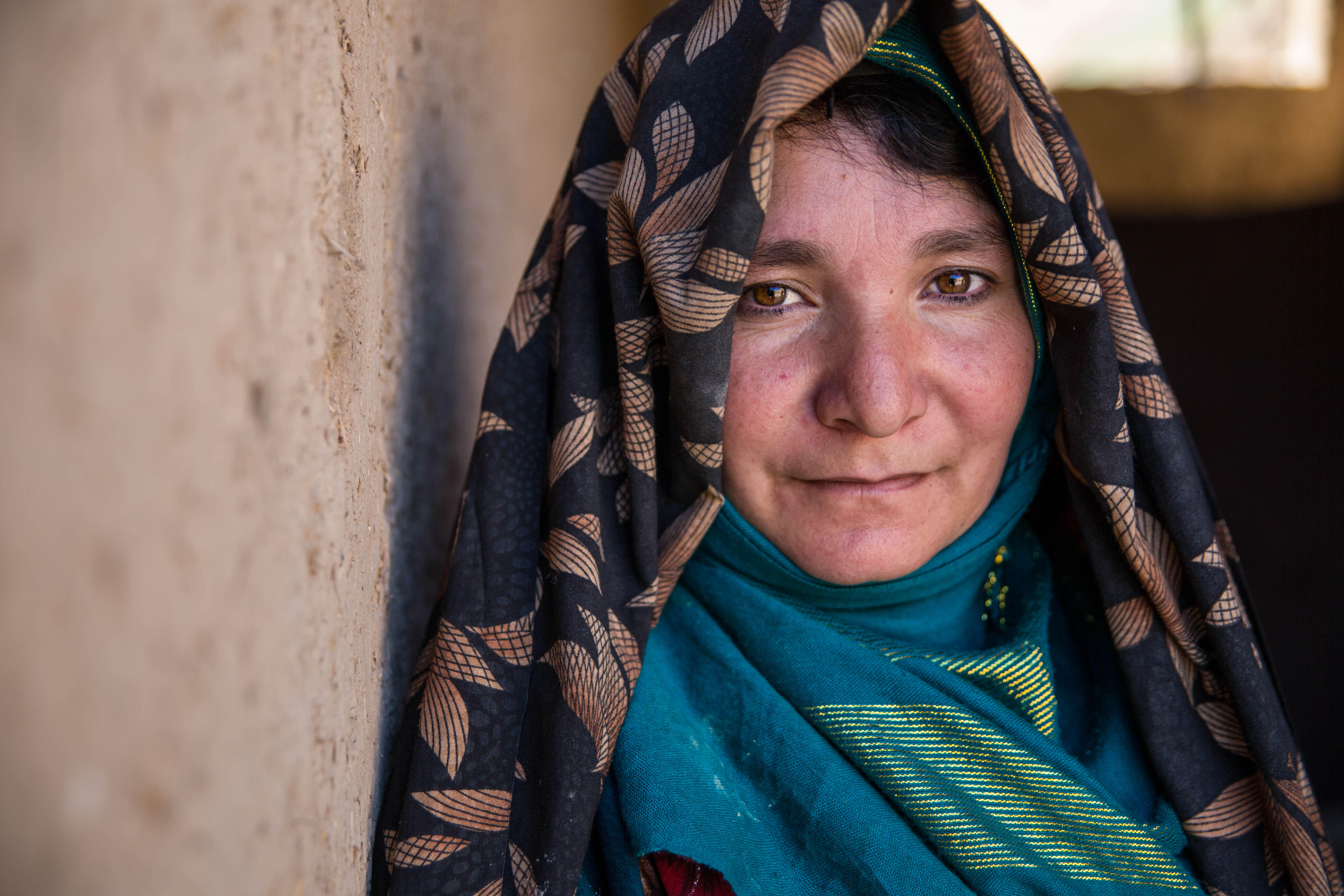 An Afghan woman looks at the camera while standing against a wall