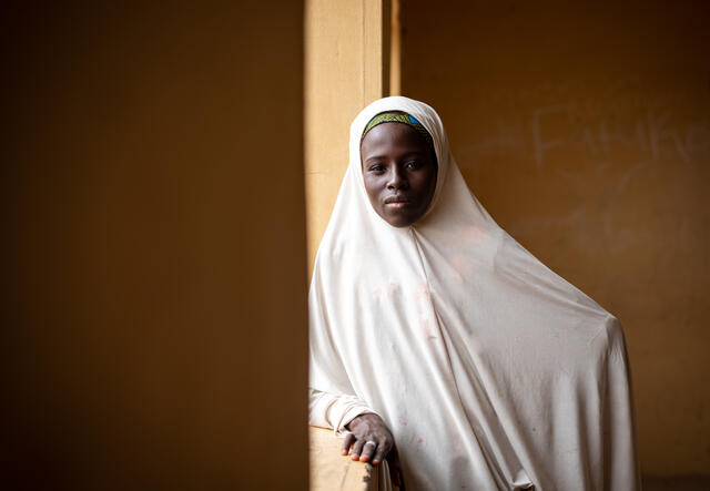 Fatima stands and looks into the camera against an orange background