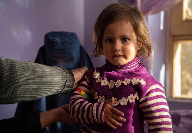 Ein Mädchen schaut in die Kamera. Jemand misst ihr ihren Arm.