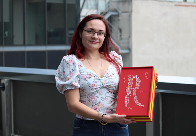 A woman stands holding a red and yellow box.