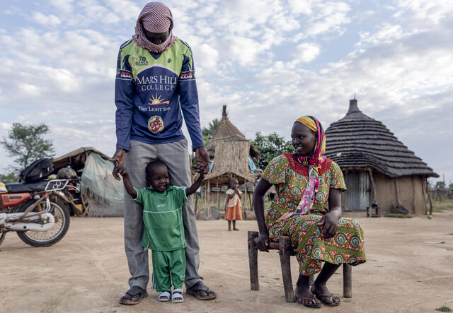 Peter stands next to his mother and father outside of their home in South Sudan.