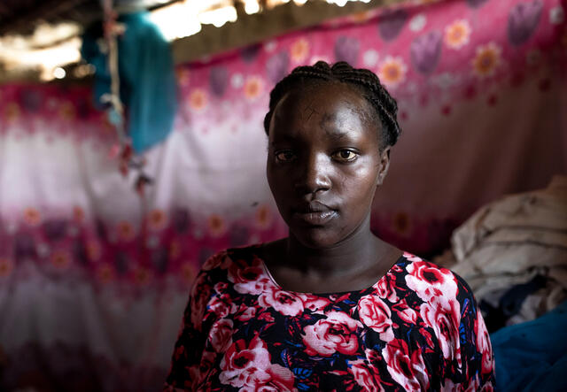A woman poses for a portrait in a dimly lit room. She looks solemnly into the camera.