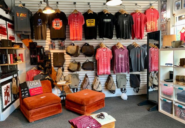 A clothing store wall featuring Created 2 Be Noticed t-shirts and backpacks