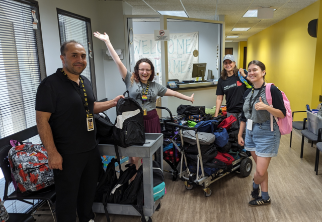 3 IRC Staff and a volunteer standing among a large collection of donated backpacks and school supplies in the IRC Atlanta lobby.