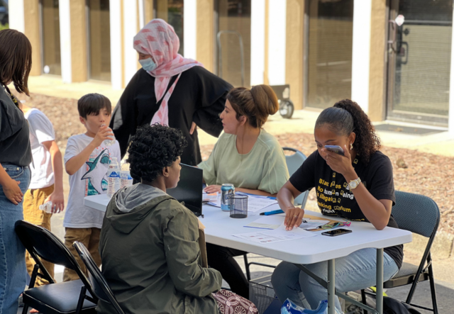 Parents, students and IRC staff seated at a table outside registering for classes.