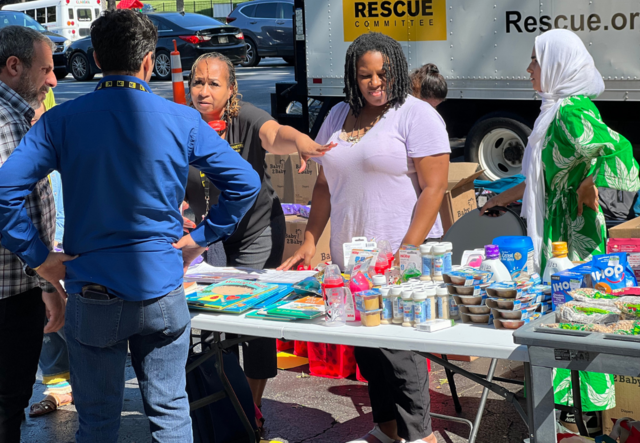IRC staff gathered around a table of donated food, baby items and school supplies.