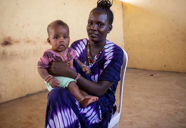 한 엄마가 의자에 앉아 어린 딸을 안고 사진 촬영을 위해 포즈를 취하고 있습니다.