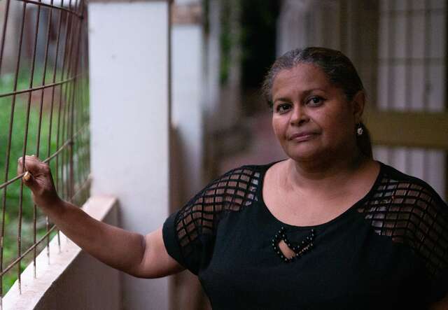 A middle aged woman poses for a photo outside of a home.