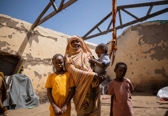 En familj i Sudan står vid sin bostad som saknar tak.