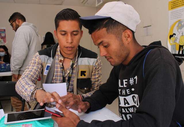 An IRC staff member shows a man how to navigate the complex CBP one app on his phone.