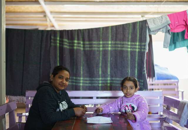 A mother and daughter sit across from each other at a table and smile for a photo.