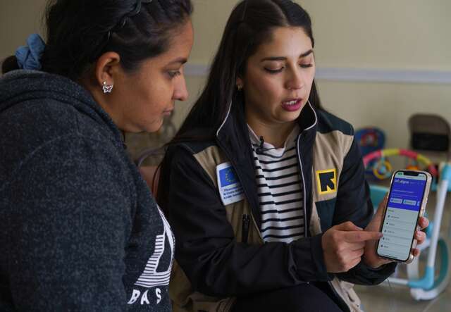 An IRC staff member shows a woman how to navigate an IRC resource on her phone.