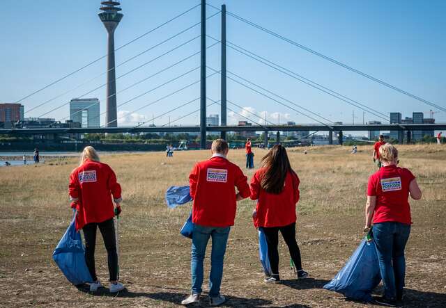 Mitarbeiter*innen der Deutschen Postcode Lotterie engagieren sich bei einer „Clean-Up“-Aktion am Ufer des Rheins. © Deutsche Postcode Lotterie