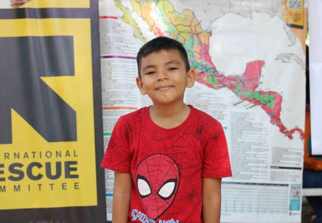 An eight-year-old boy smiles and poses for a photo next to an IRC logo.