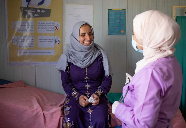 Eine syrische Frau sitzt in einer Notunterkunft während einer medizinischen Beratung mit einer Gesundheitshelferin, die sie unterstützt.