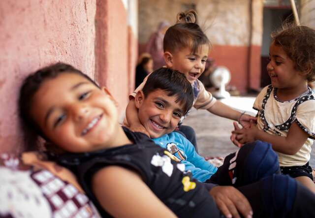 Eine Gruppe syrischer Kinder spielt lachend zusammen in einer Notunterkunft.