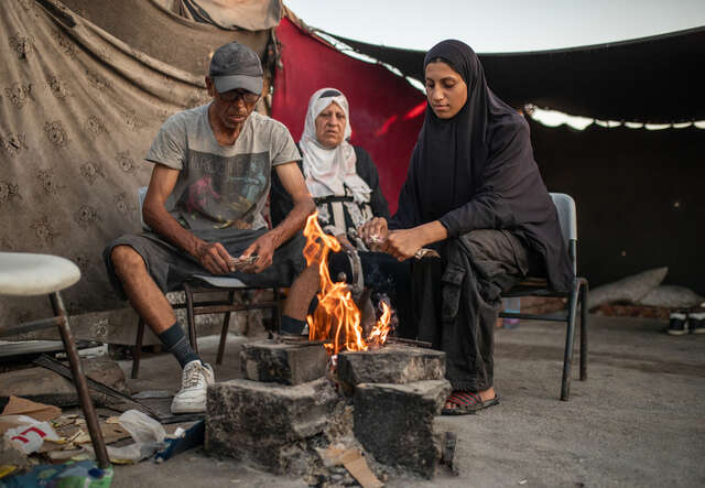 Tonårsflicka i Gaza med sina föräldrar sitter vid en öppen eld där flickan lagar mat.