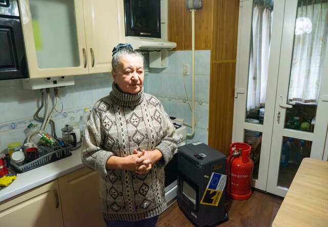 Eine ältere Frau steht in ihrem Haus in der Ukraine neben einem von IRC bereitgestellten Gasherd.