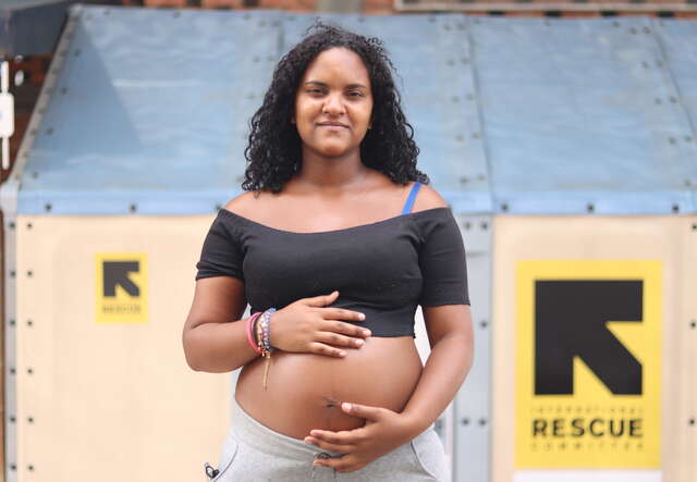 Gravid kvinna i Colombia håller två händer om sin mage framför en vägg med RESCUE:s logga.
