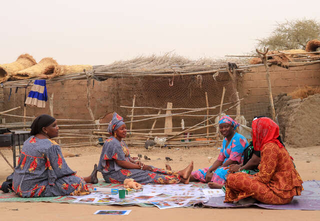 Fem kvinnor i Mali sitter utomhus på filtar med informationsmaterial om amning.