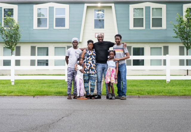 A family hugs and smiles in front of their home