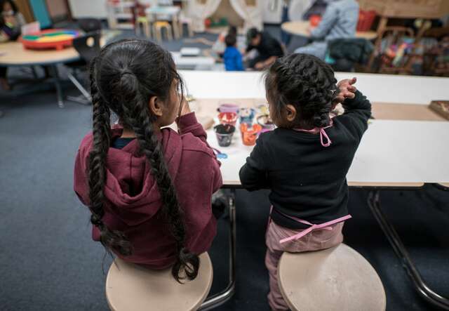 Two girls sit at a table and do an arts and crafts activity together.